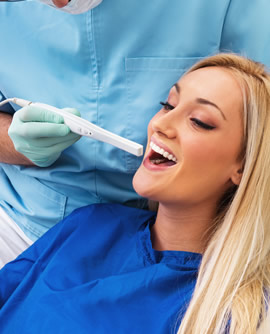 A woman sitting in a dental chair, opens her mouth as a dentist holds an intraoral camera in front of her.